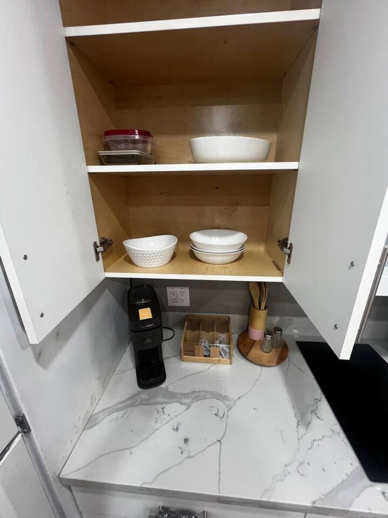 Una cocina con cafetera, salerosos y pimenteros, además de un caja de almacenamiento en la encimera.