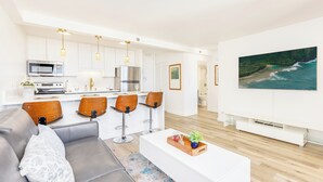 Ein modernes Wohnzimmer mit einem grauen Sofa, Holzstühlen, einem weißen Couchtisch und einem großen Gemälde, das eine Strandansicht zeigt.
