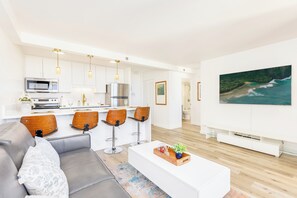 Ein modernes Wohnzimmer mit einem grauen Sofa, Holzstühlen, einem weißen Couchtisch und einem großen Gemälde, das eine Strandansicht zeigt.