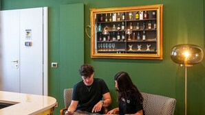 Two people seated on a patterned sofa, a bar area with liquor bottles, and a green wall. - CasaJammone Up Boutique Rooms (Naples)