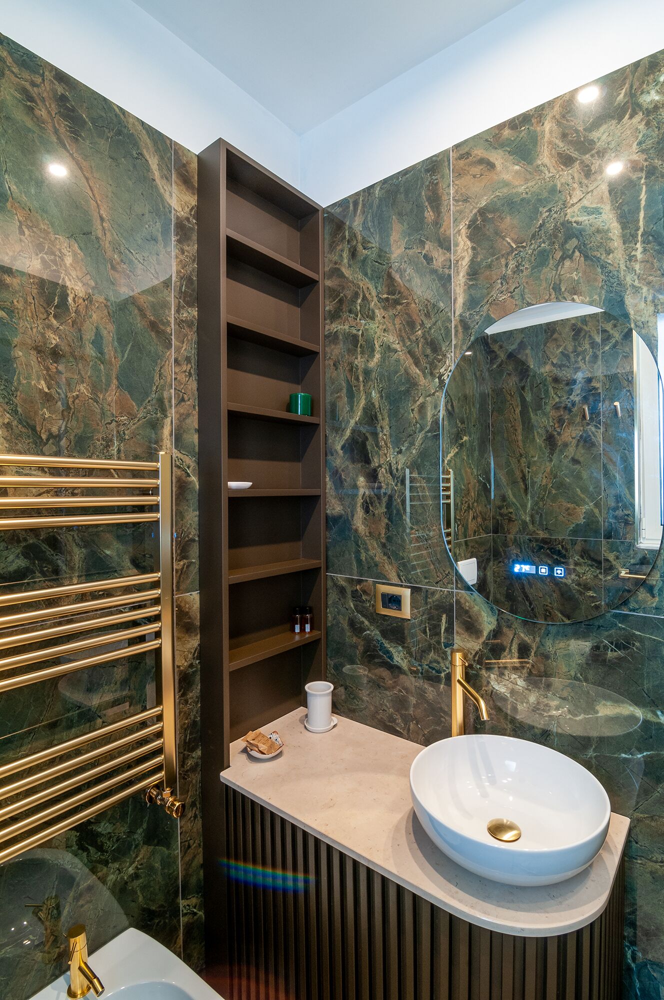 Un baño moderno con pared de mármol, estante empotrado, tocador con lavamanos y toallero.