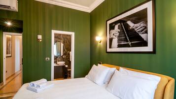 A hotel room with a bed, a framed photograph on the wall, a bathroom visible through an open door, and a wall-mounted air conditioning unit.