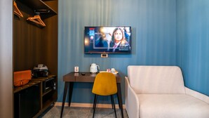 A room with a television mounted on the wall displaying a program, a desk with a chair, a coffee machine, and a small table with a teapot and cups. - CasaJammone Up Boutique Rooms (Naples)
