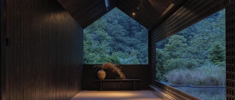 A room with a wooden floor, a bench, and a large window overlooking a forest.