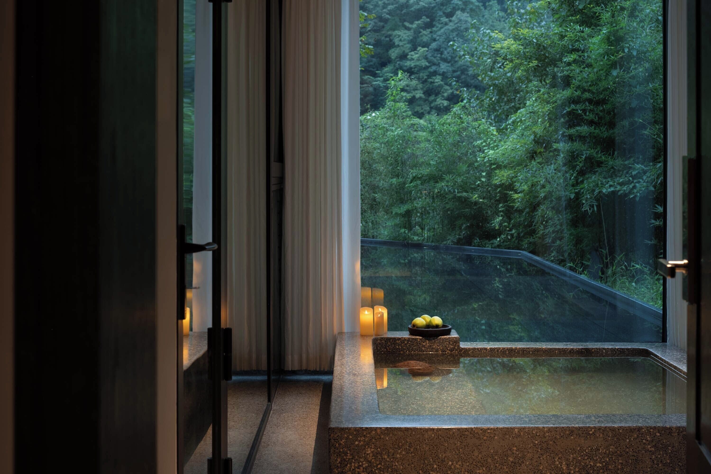 A spa area with a hot tub, candles, and a view of a forest.