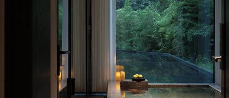 A spa area with a hot tub, candles, and a view of a forest.