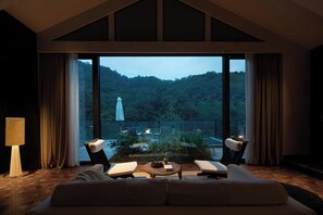 A spacious living room with a large window, a sofa, two armchairs, a coffee table, and a lamp.