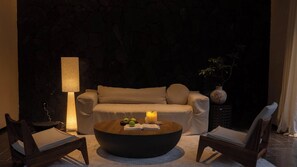 A cozy seating area with a sofa, two chairs, a coffee table with apples and a book, a lamp, and a vase.