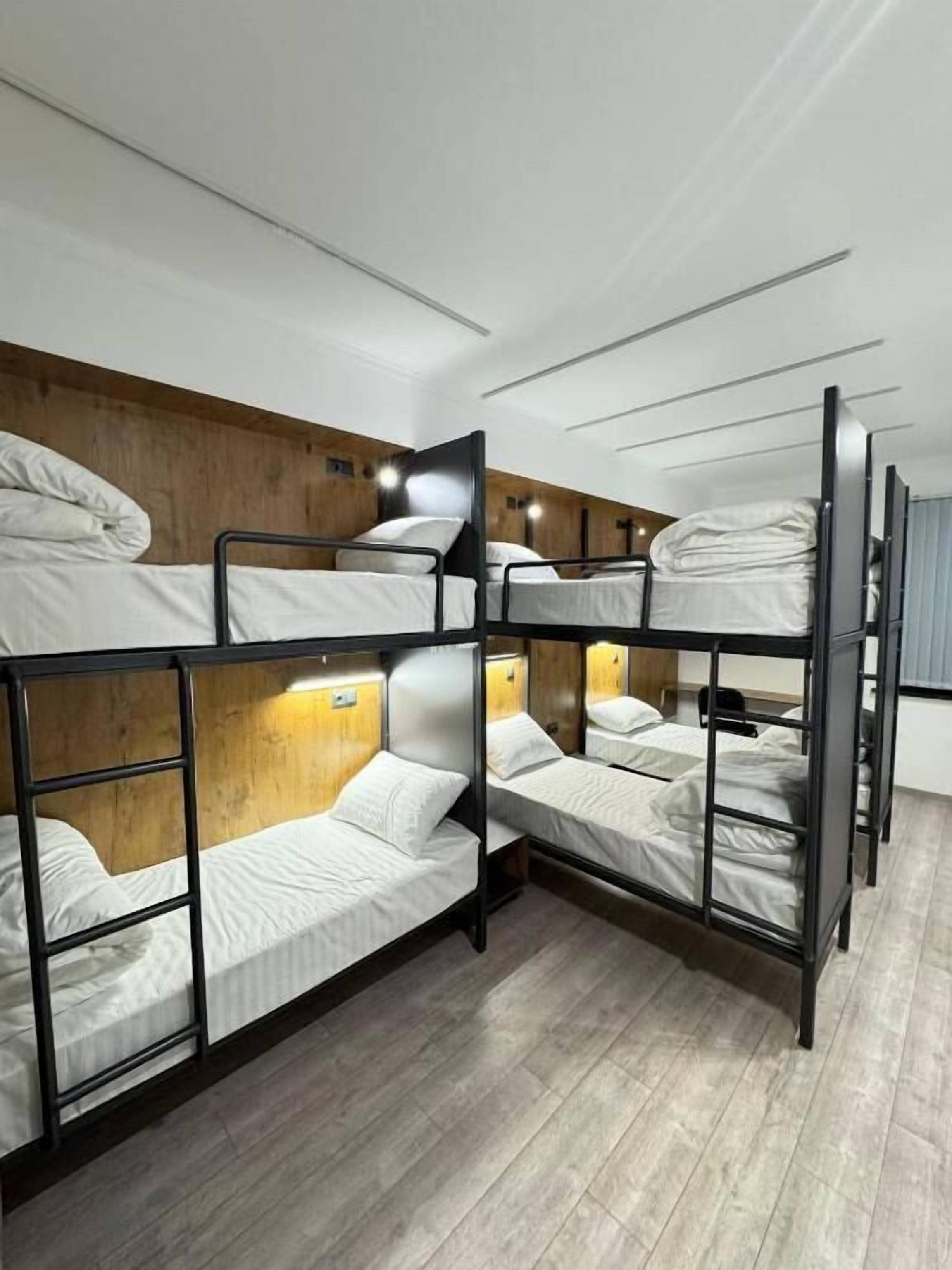 A bunk bed room with wooden headboards, a light fixture, and a wooden floor.