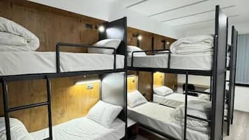 A bunk bed room with wooden headboards, a light fixture, and a wooden floor.