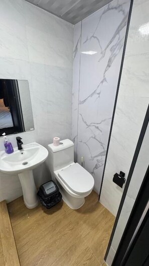 A bathroom with a white sink, toilet, and bidet, marble wall tiles, and a wooden floor.