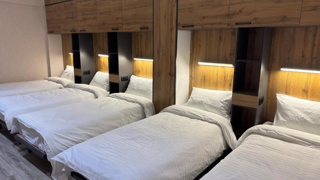 A hotel room with four beds arranged in a row, wooden headboards, and built-in lighting.