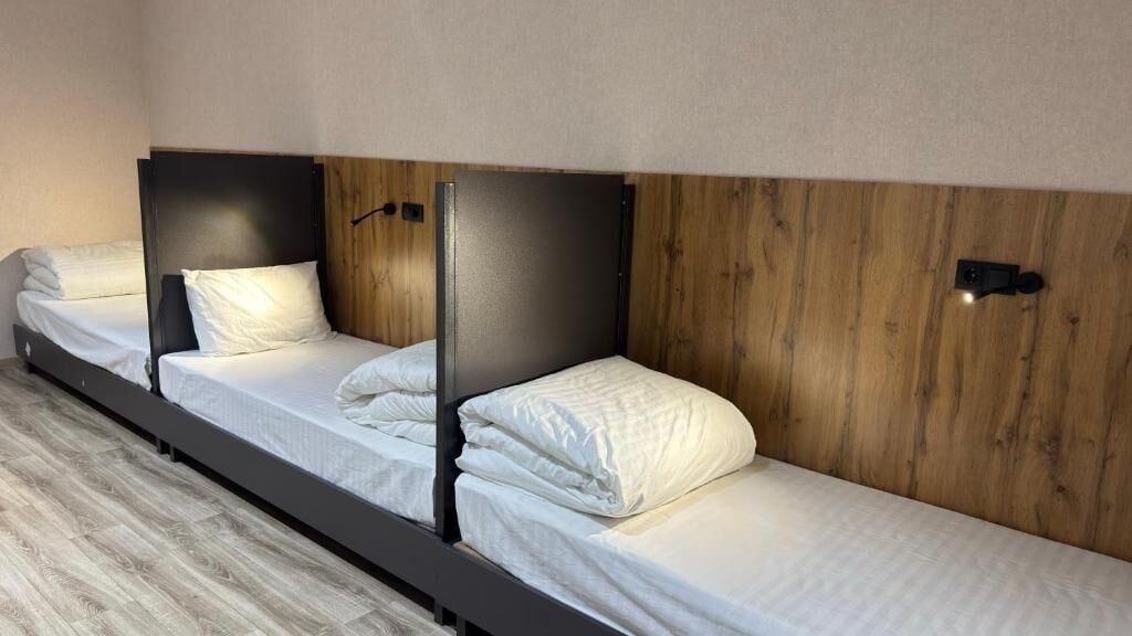 A hotel room with three single beds aligned against a wooden wall.