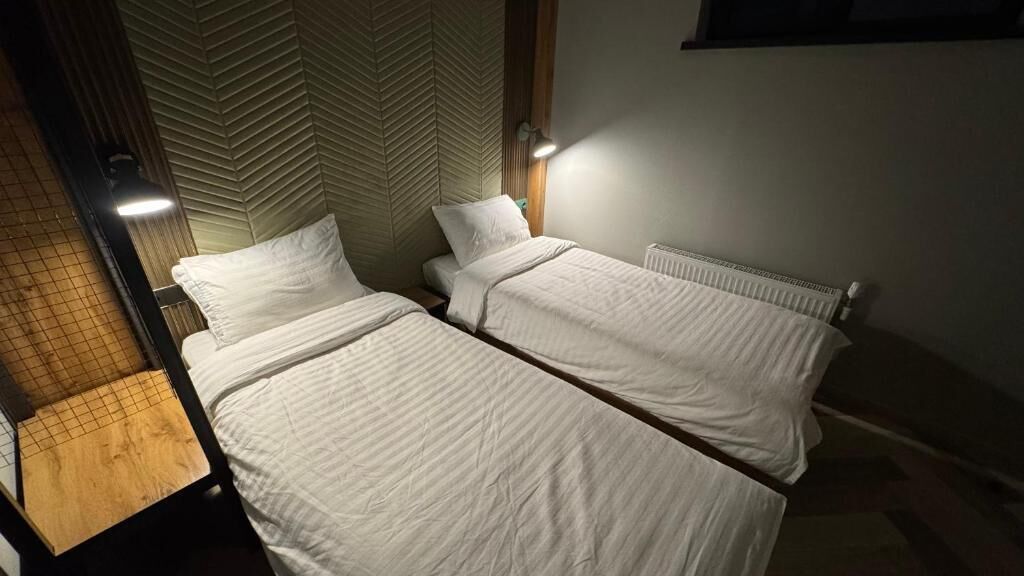 Quarto com duas camas, um radiador e uma parede com padrão geométrico.