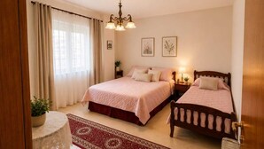 A hotel room with two beds, a chandelier, a red patterned rug, and a small table with a lace tablecloth. - Nilvan Apartment heart of Tirana (Tiranë)