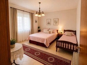 Ein Hotelzimmer mit zwei Betten, einer Kristallleuchter, einem roten Teppich mit Muster und einem kleinen Tisch mit weißer Spitzenleinentischdecke.