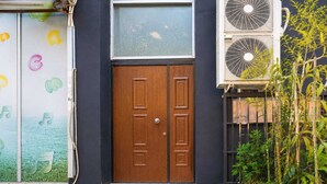 A wooden double door with a window above it, a brick-paved entrance, and a garden with bamboo plants. - Nilvan Apartment heart of Tirana (Tiranë)