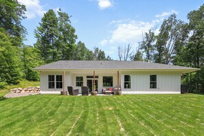 A single-story house with a covered porch, a stone wall, and a lawn.