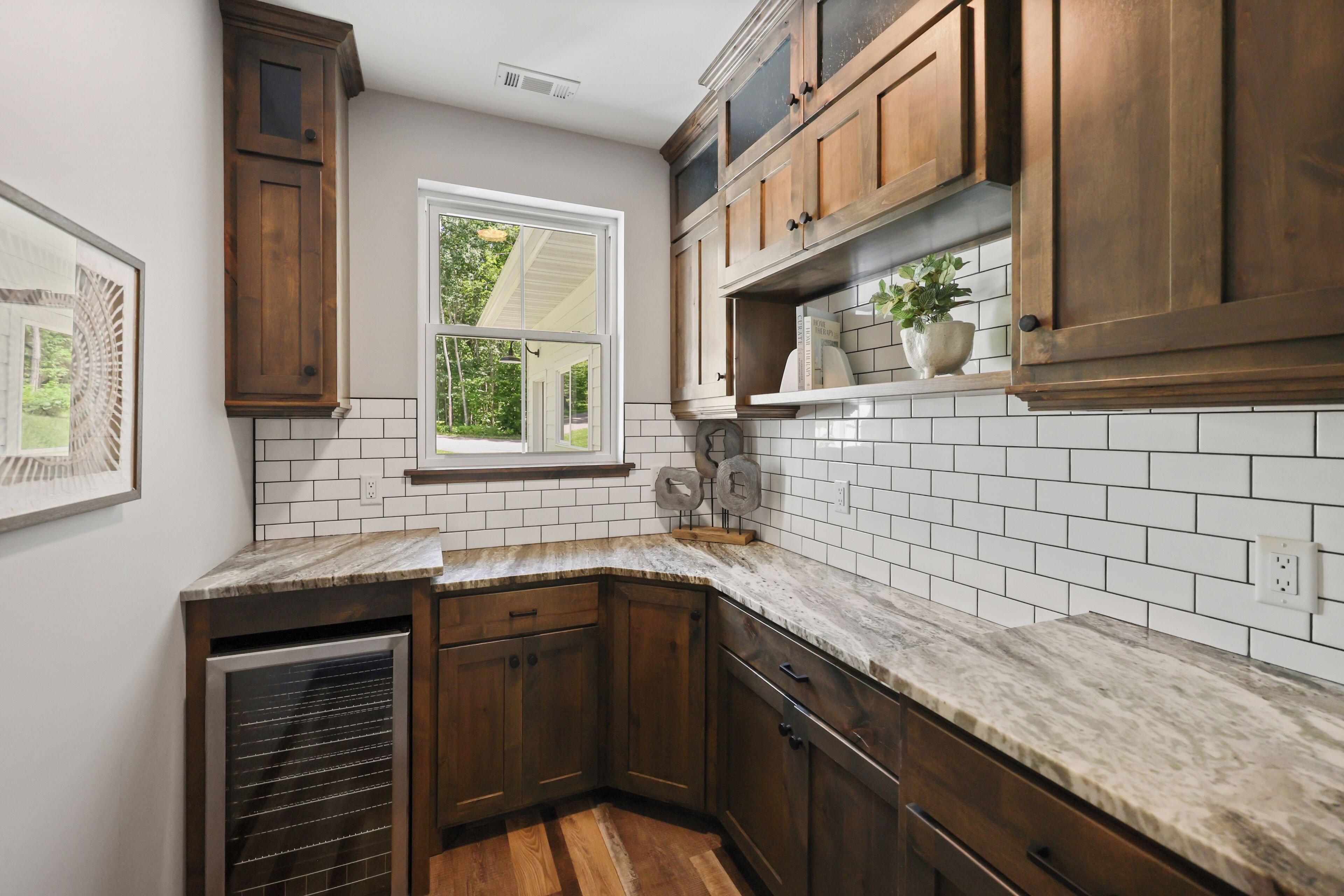 A kitchen with wooden cabinets, white subway tiles, and a window overlooking greenery.