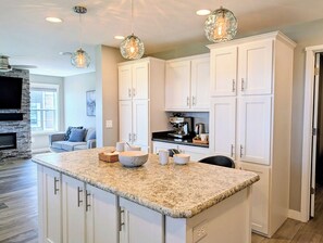 A kitchen with white cabinets, a granite countertop, and a stone fireplace. - 22 South Shore Drive Ext - South Shore Marina (Bethany Beach)