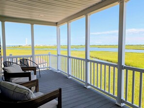 Eine überdachte Veranda mit weißen Geländern, Blick auf ein Gewässer und eine grüne Landschaft.