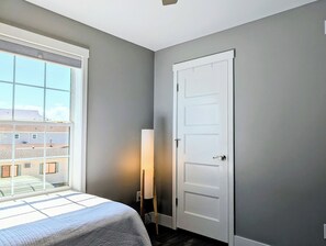 Ein Zimmer mit einem Bett, einem Fenster, einer Tür und einer Stehlampe.