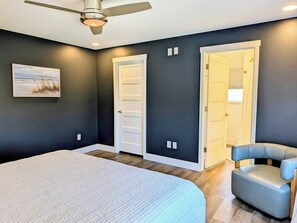 A bedroom with a bed, a ceiling fan, two doors, a chair, and a painting on the wall. - 22 South Shore Drive Ext - South Shore Marina (Bethany Beach)
