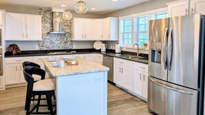 A modern kitchen with white cabinets, a central island, stainless steel appliances, and pendant lighting.