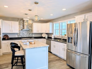 A modern kitchen with white cabinets, a central island, stainless steel appliances, and pendant lighting. - 22 South Shore Drive Ext - South Shore Marina (Bethany Beach)