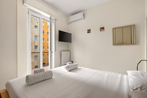 A hotel room with a bed, a TV, a radiator, and a view of a building through an open door. - Authentic North Milan · Metro M3 · Park · A/C · Self-check-in (Milano)