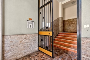 A staircase with a metal gate leading to a room with a brick wall and a control panel on the wall. - Authentic North Milan · Metro M3 · Park · A/C · Self-check-in (Milano)