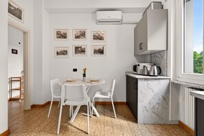 Une cuisine moderne dotée d’un plan de travail en marbre, de meubles blancs et d’un coin repas avec des chaises blanches.