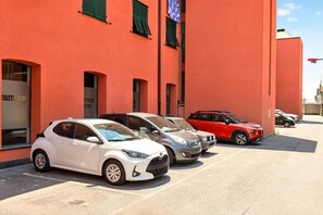 A parking lot with several cars parked in front of a building with green shutters and a red facade. - Spacious and bright penthouse, ideal for up to 7 people (Genova)