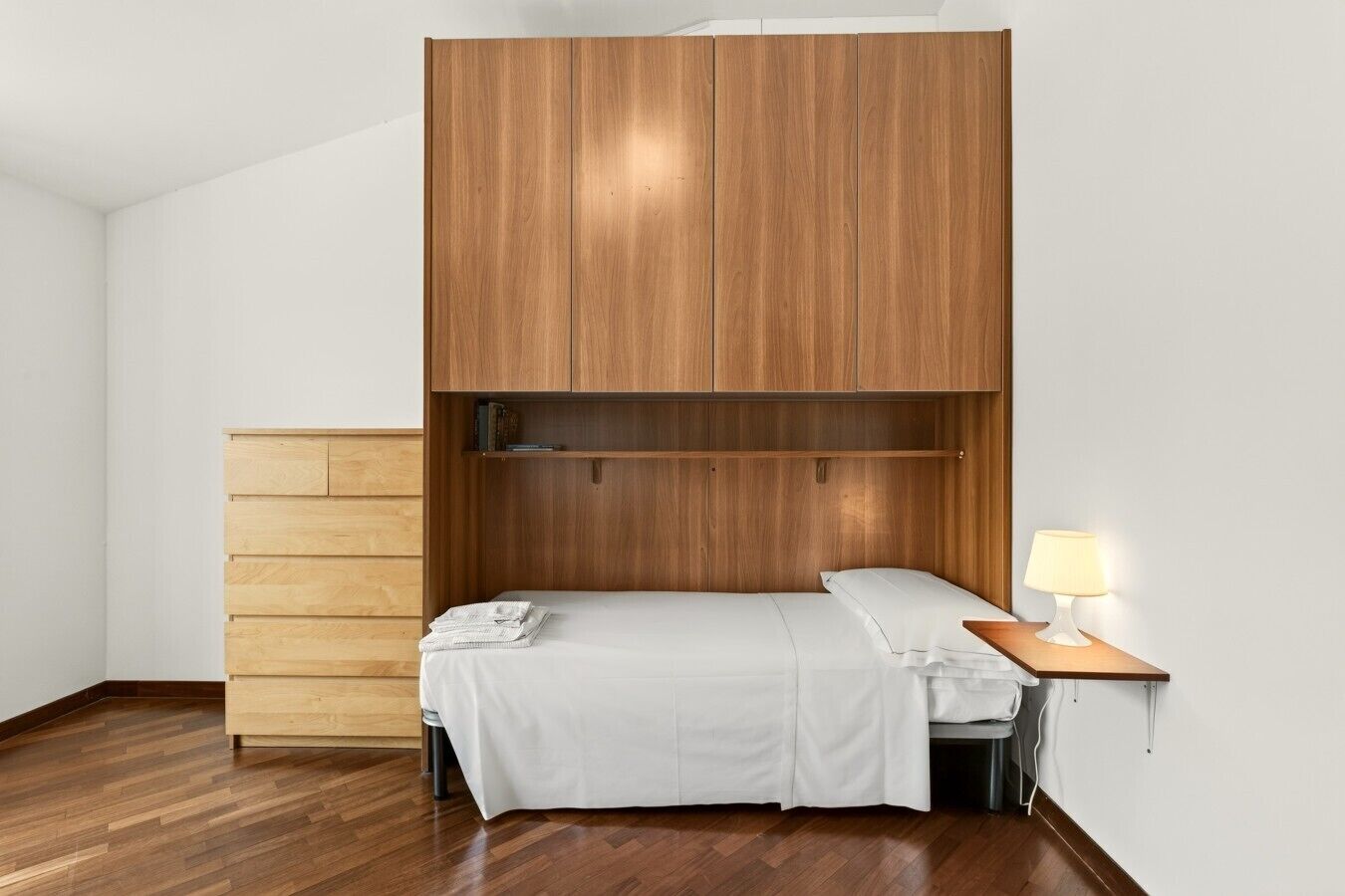 Quarto com cama, mesa de cabeceira, abajur e guarda-roupa de madeira.