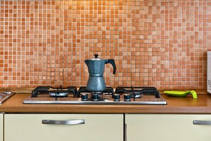 A kitchen with a gas stove, a coffee pot, and a tiled backsplash. - Spacious and bright penthouse, ideal for up to 7 people (Genova)