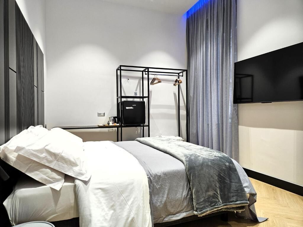 A modern hotel room with a bed, a bedside table, a TV mounted on the wall, and a window with curtains.