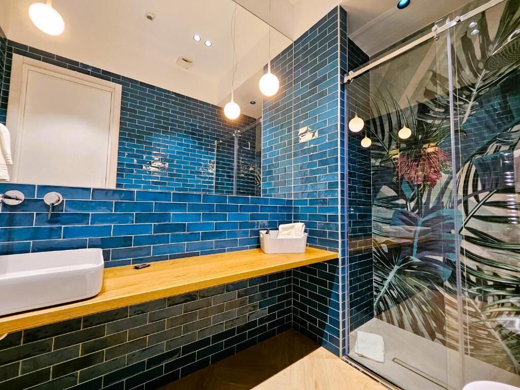 Un bagno con una parete rivestita in piastrelle blu, un piano d'appoggio in legno, un lavandino bianco e un box doccia in vetro.