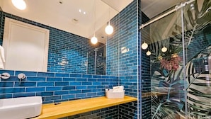Ein Badezimmer mit blauen Fliesen, einer Holzauskleidung, einem weißen Waschbecken und einer Duschkabine aus Glas.