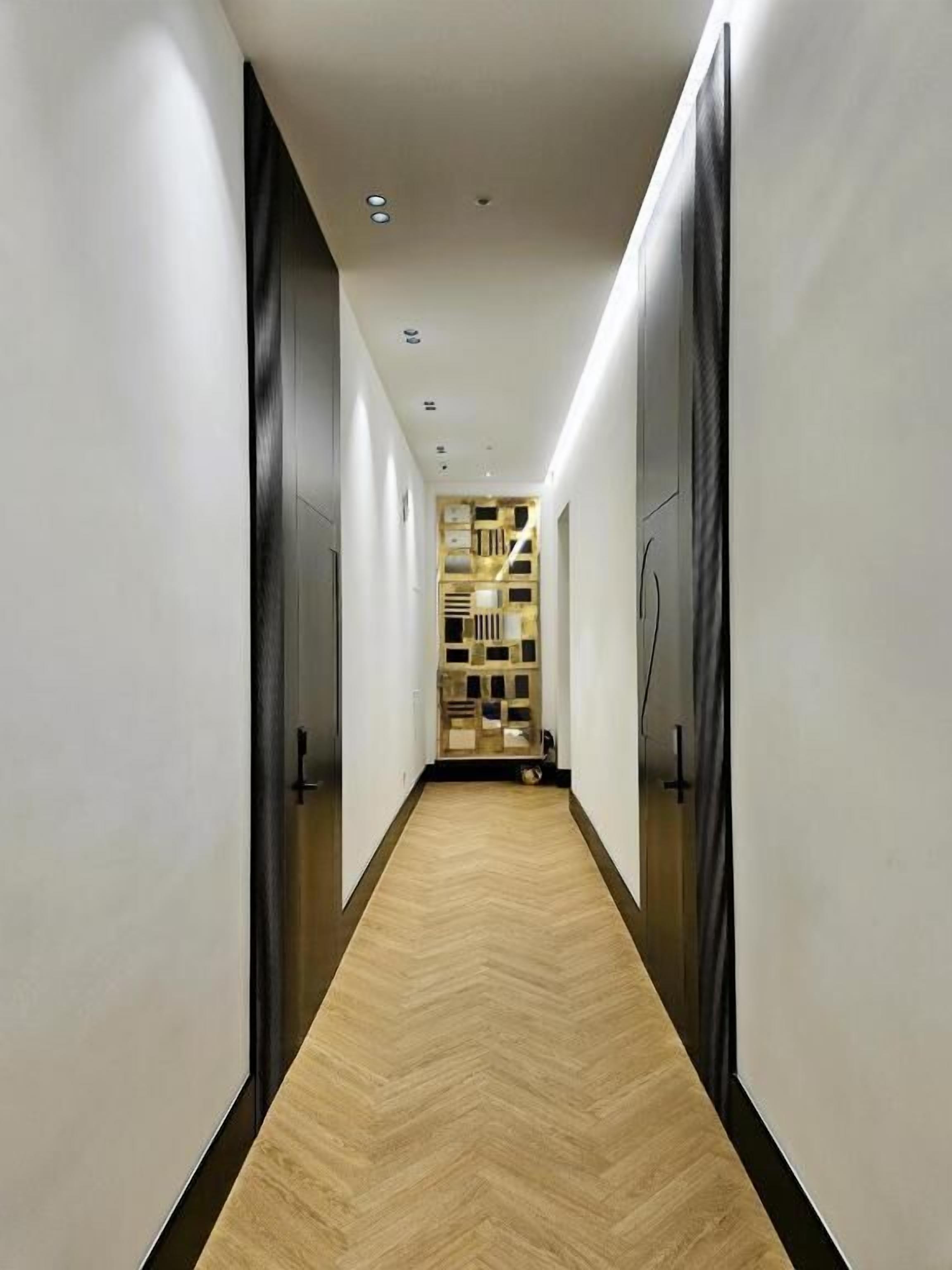 A hallway with a wooden floor, white walls, and a black door at the end.