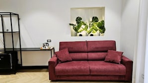 Ein rotes Sofa mit Kissen, ein schwarzes Metallregal und eine Wandpflanze.