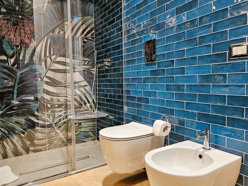 A bathroom with a blue tiled wall, a glass shower enclosure, a toilet, and a sink.