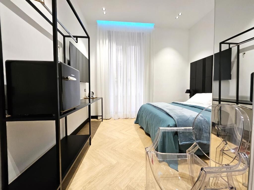 Een moderne hotelkamer met een bed, een televisie op een zwart voetstuk, een bureau met stoel, en een groot raam met dunne gordijnen.