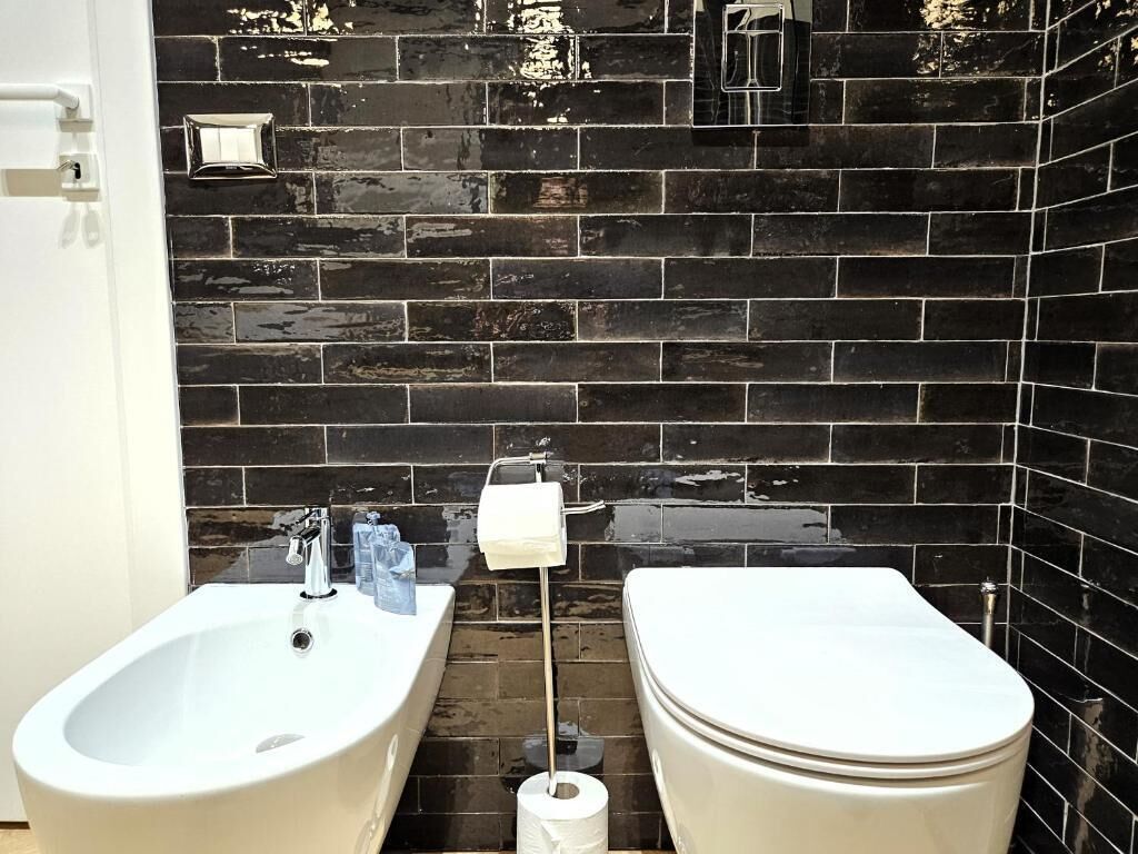 Un bagno con una vasca da bagno bianca, un lavandino bianco e un water su un muro rivestito di piastrelle nere.