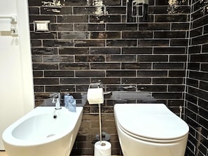 A bathroom with a white bathtub, a white sink, and a toilet against a black tiled wall. - Orefici Place (Naples)
