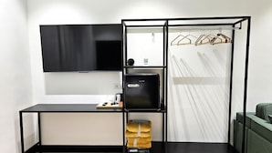 Ein gemütlicher Raum mit einem schwarzen Schreibtisch, einem Flachbildfernseher, einer Minikühlschrank und einem Kleiderständer.