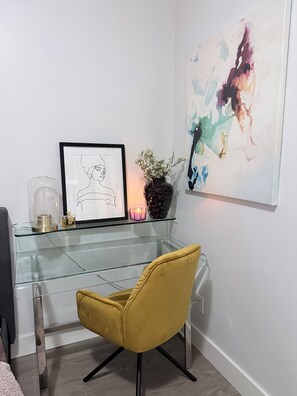 A modern room with a glass desk, a framed artwork, a vase with flowers, and a yellow chair.