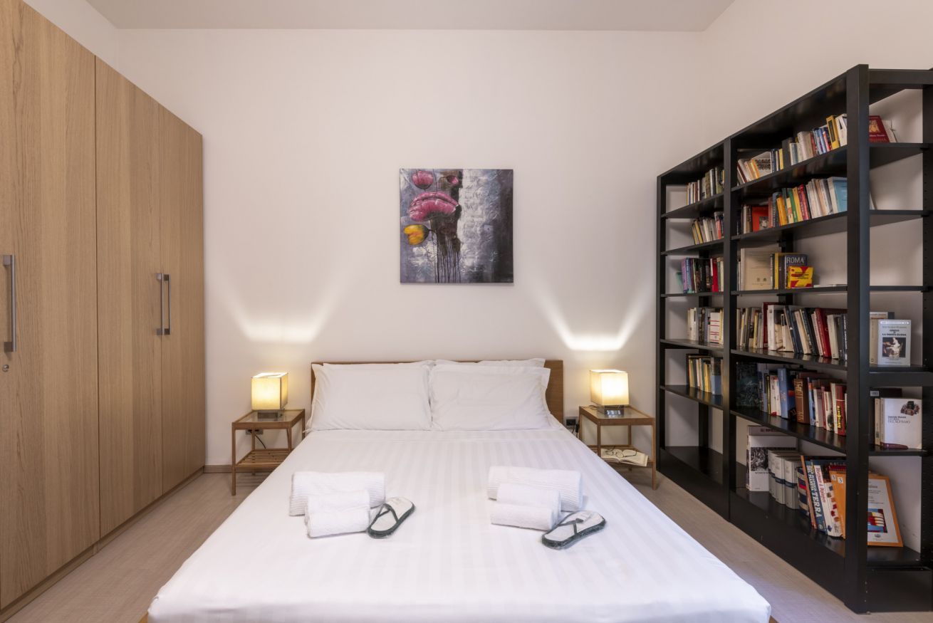 Une chambre d’hôtel avec un grand lit, deux tables de chevet, une bibliothèque et une armoire.