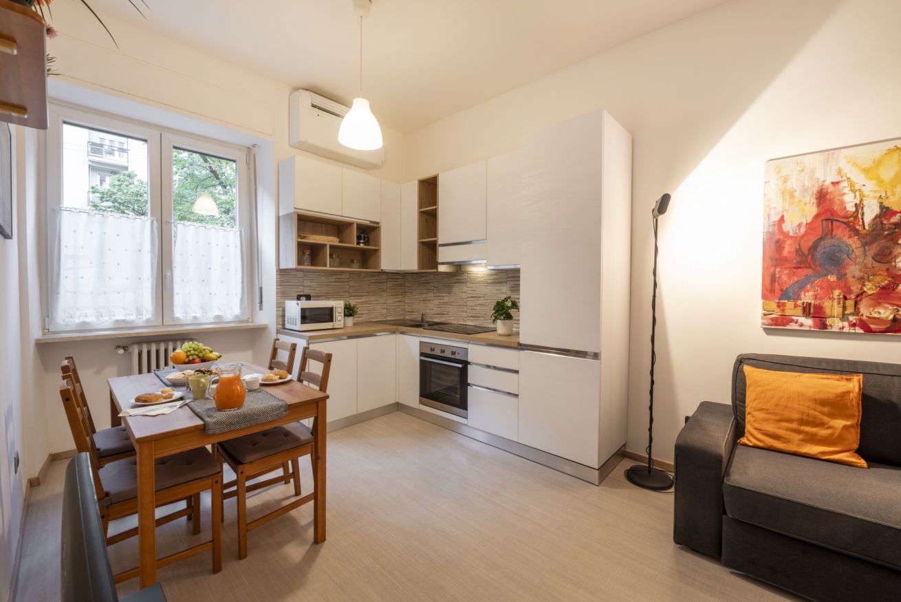 A modern kitchen with white cabinetry, a dining table with chairs, and a sofa in the living area.