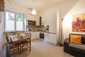 A modern kitchen with white cabinetry, a dining table with chairs, and a sofa in the living area. - STRAMBIO, 8 – Smart Stay in Milan (Milano)