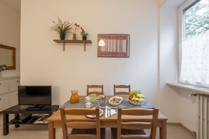 Uma área de refeições com uma mesa posta para dois, uma televisão e uma janela com vista para árvores.
